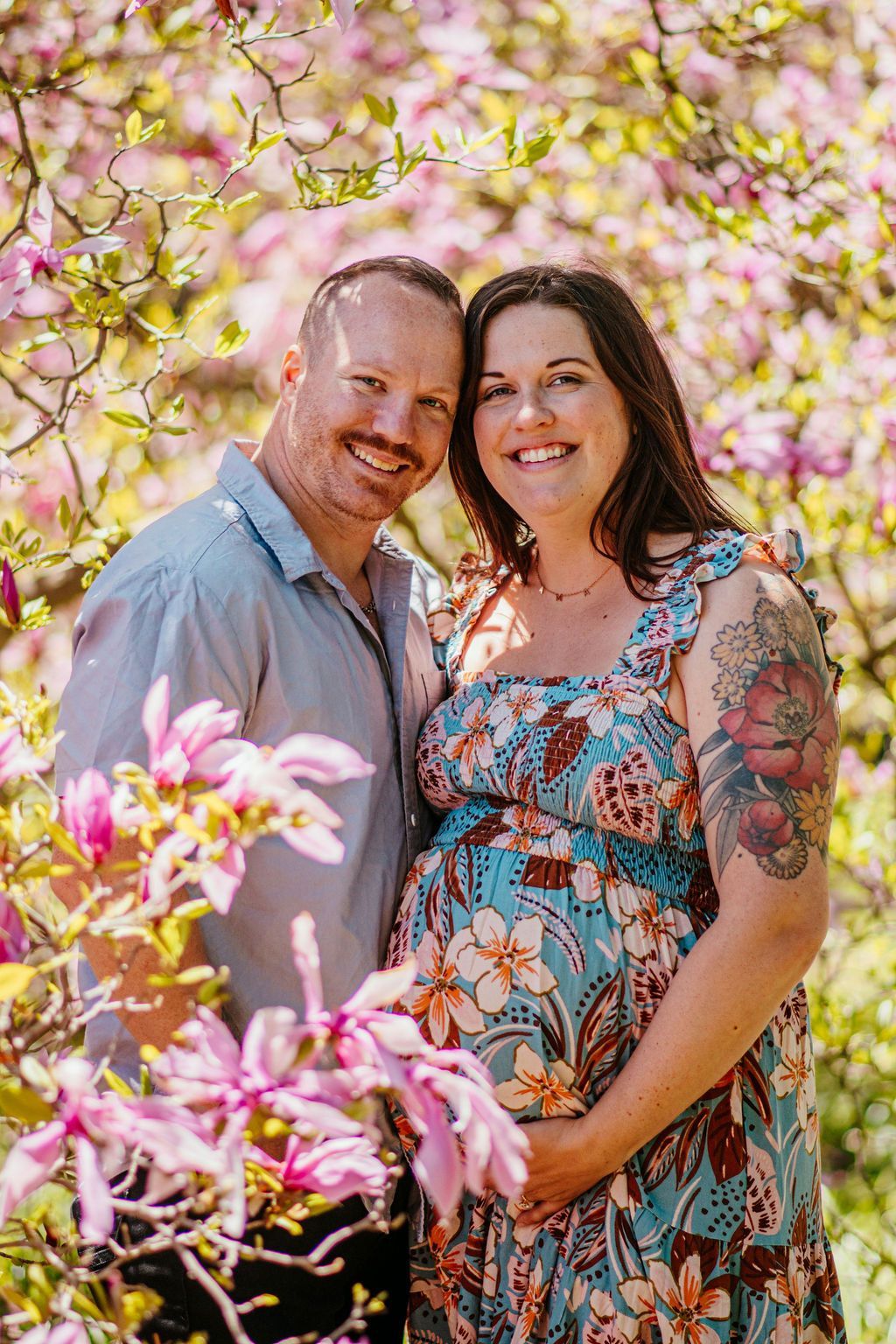 Couple smiling in colorful floral surroundings, posing outdoors among pink blossoms