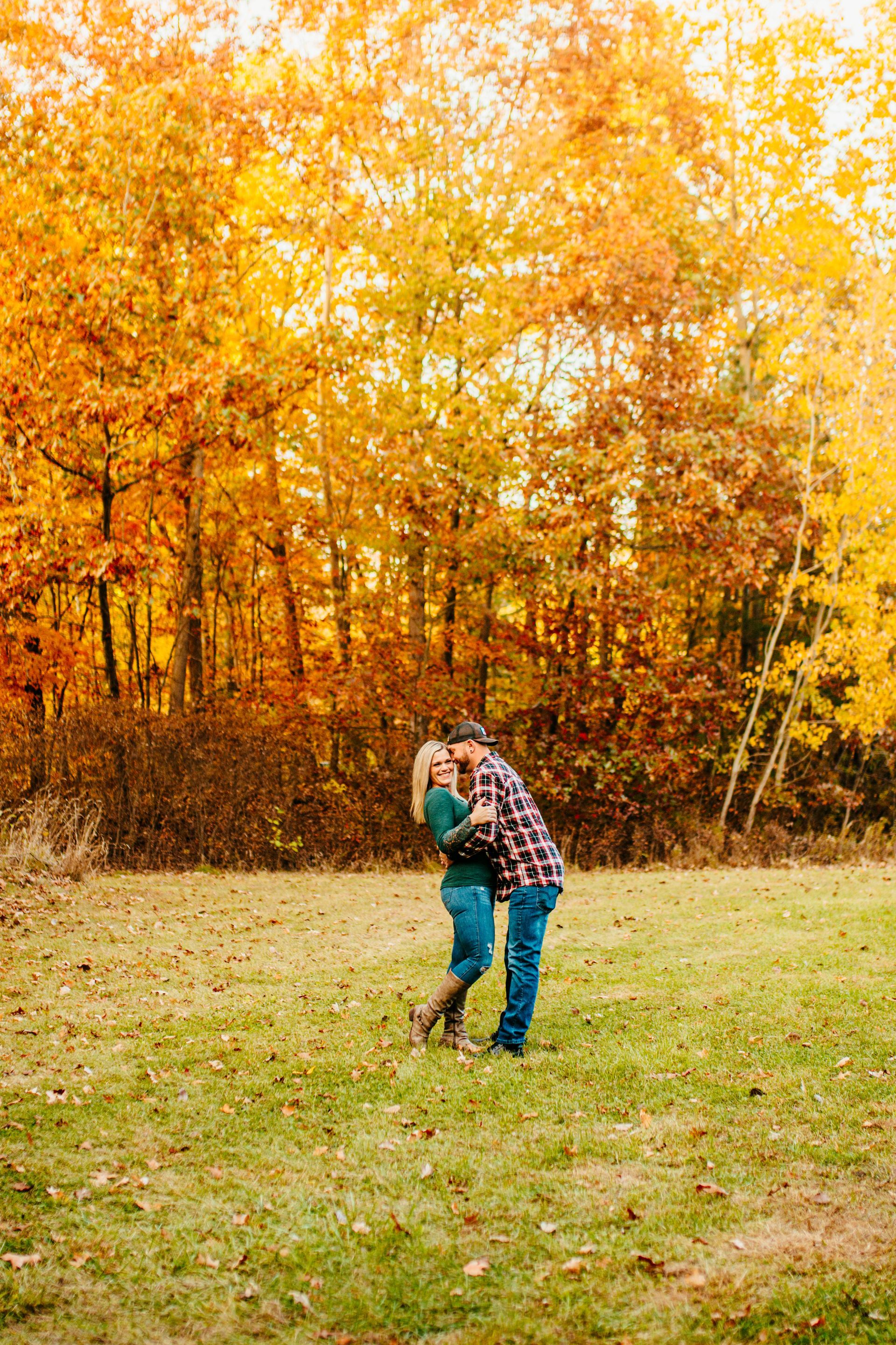 Two people embracing on a grassy field before bright autumn trees