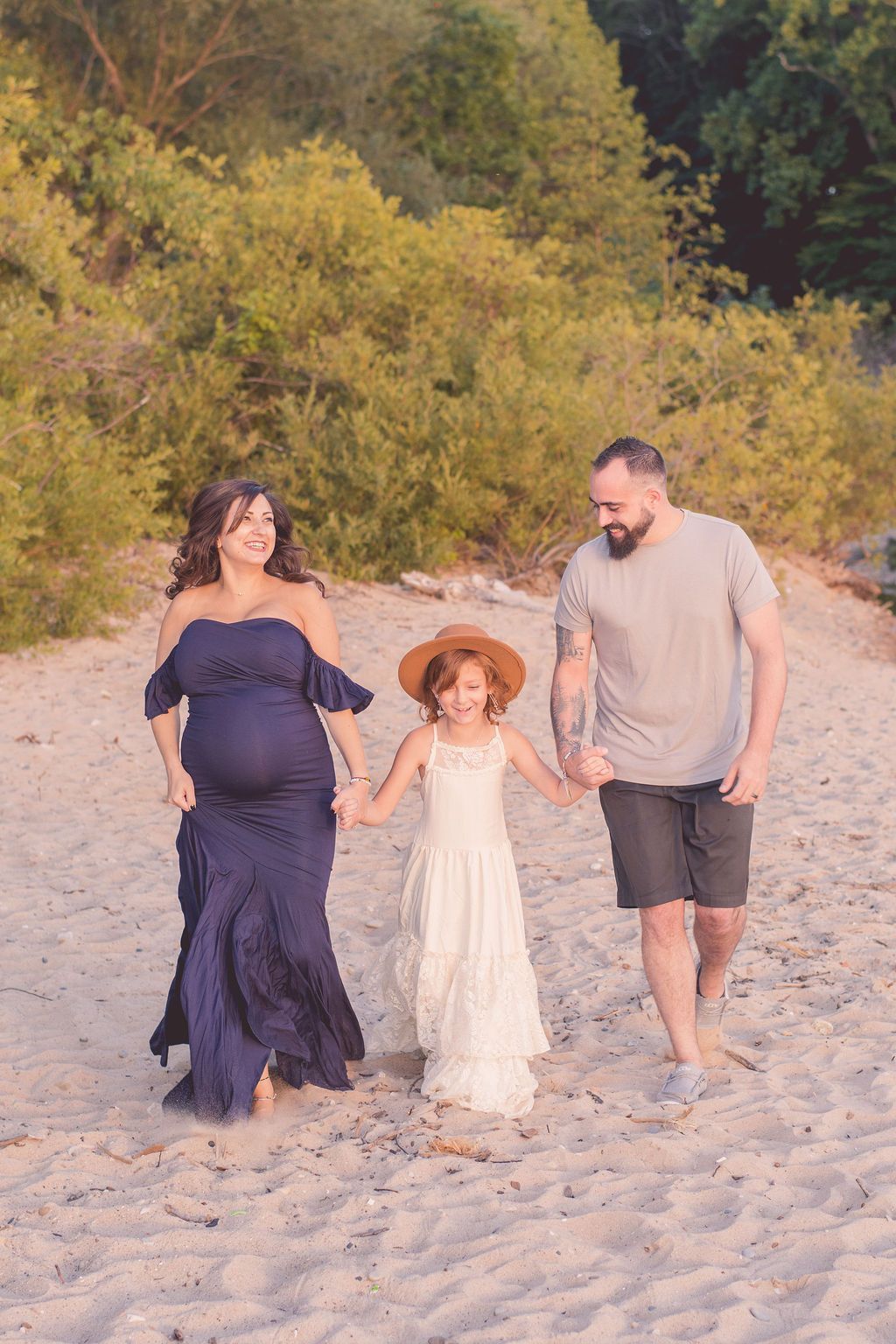 Family walking hand in hand on a sandy beach at sunset, with trees in the background.