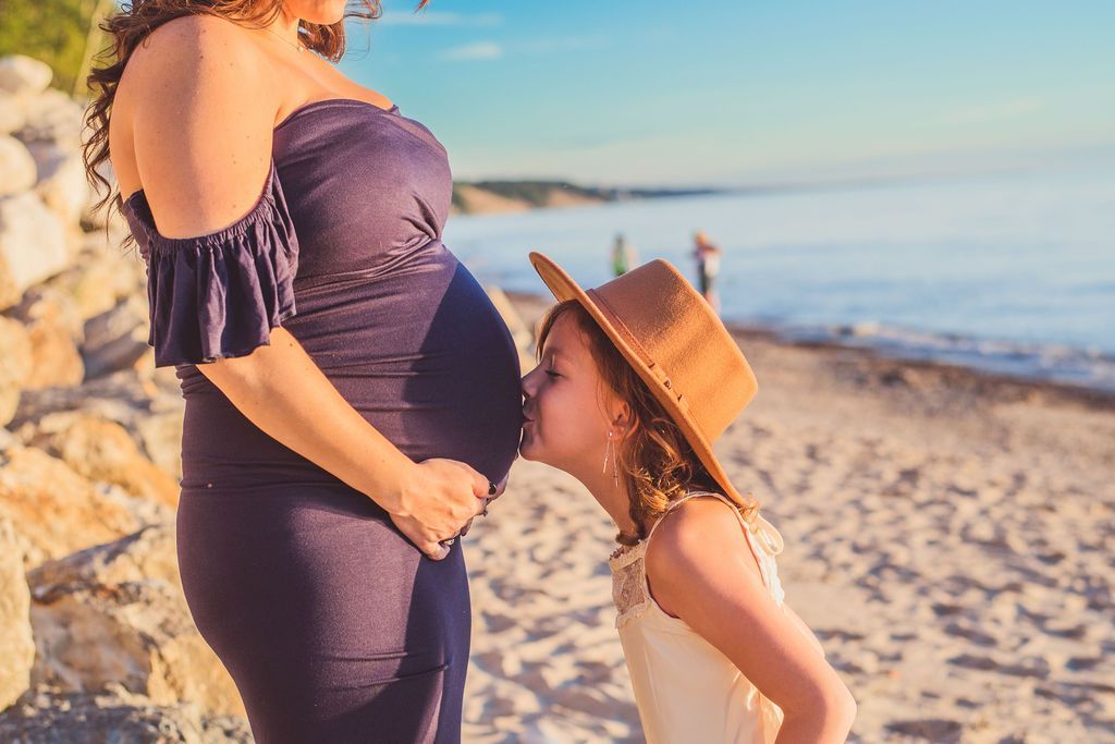 Pregnant woman on a sunny beach with a child kissing her belly