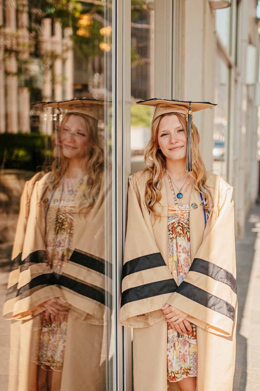 Woman in a cream floral dress and black-striped shawl standing by a glass door, with her reflection beside her