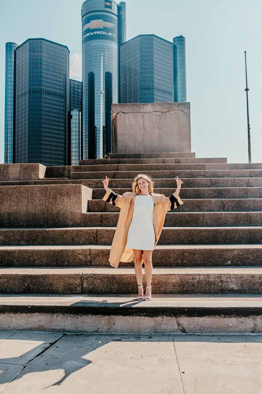 Person in a beige coat standing on steps in front of modern glass skyscrapers.