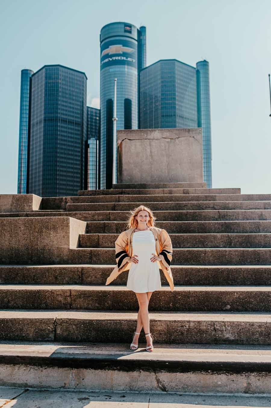 Woman in white dress standing on stone steps with modern glass skyscrapers behind her