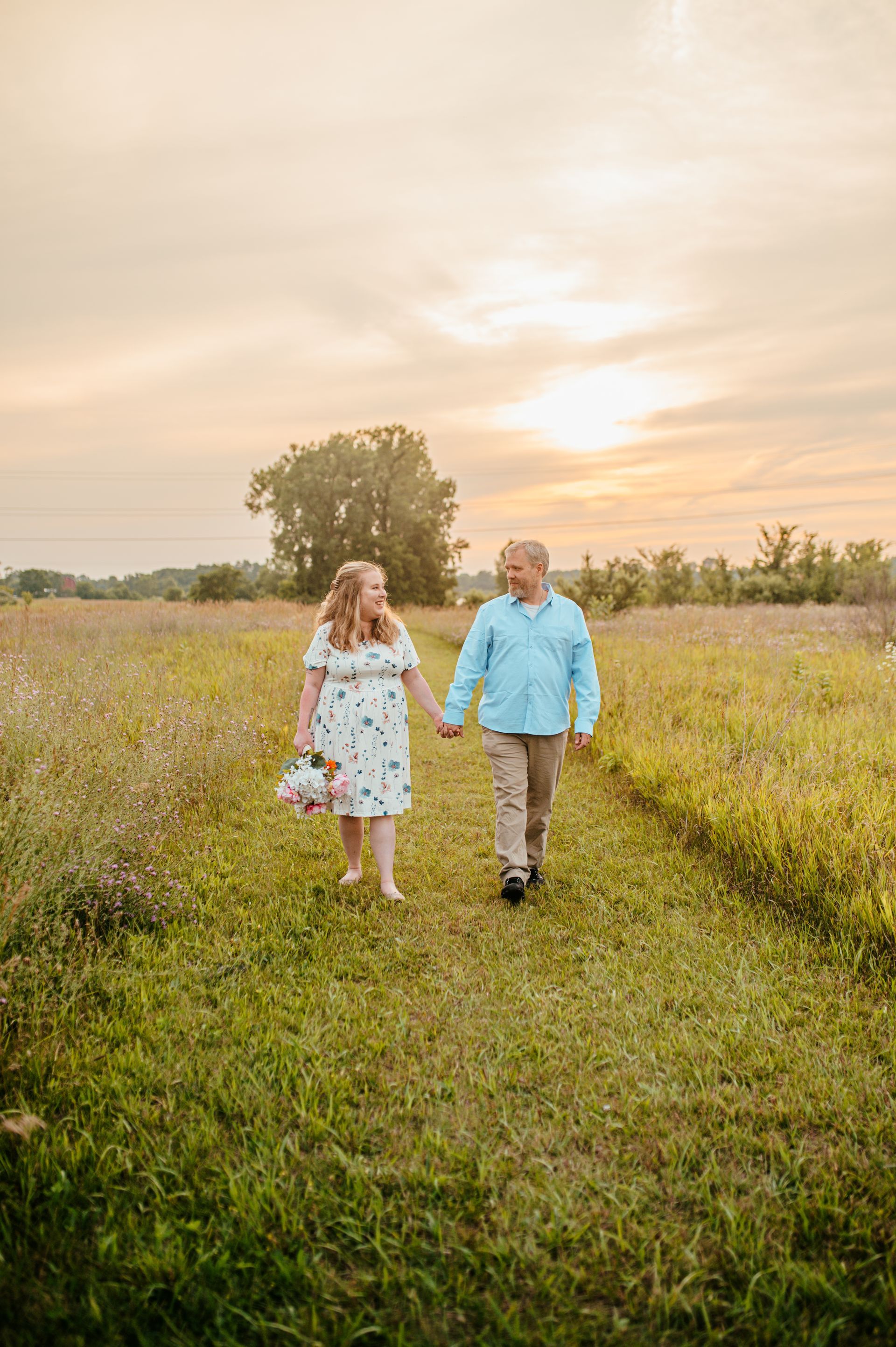 Two people walking hand in hand through a grassy field at sunset