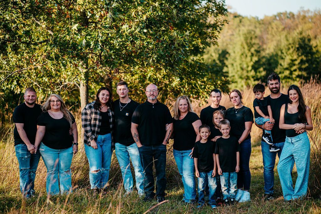 Group of people standing together outdoors in a grassy field with trees in the background.