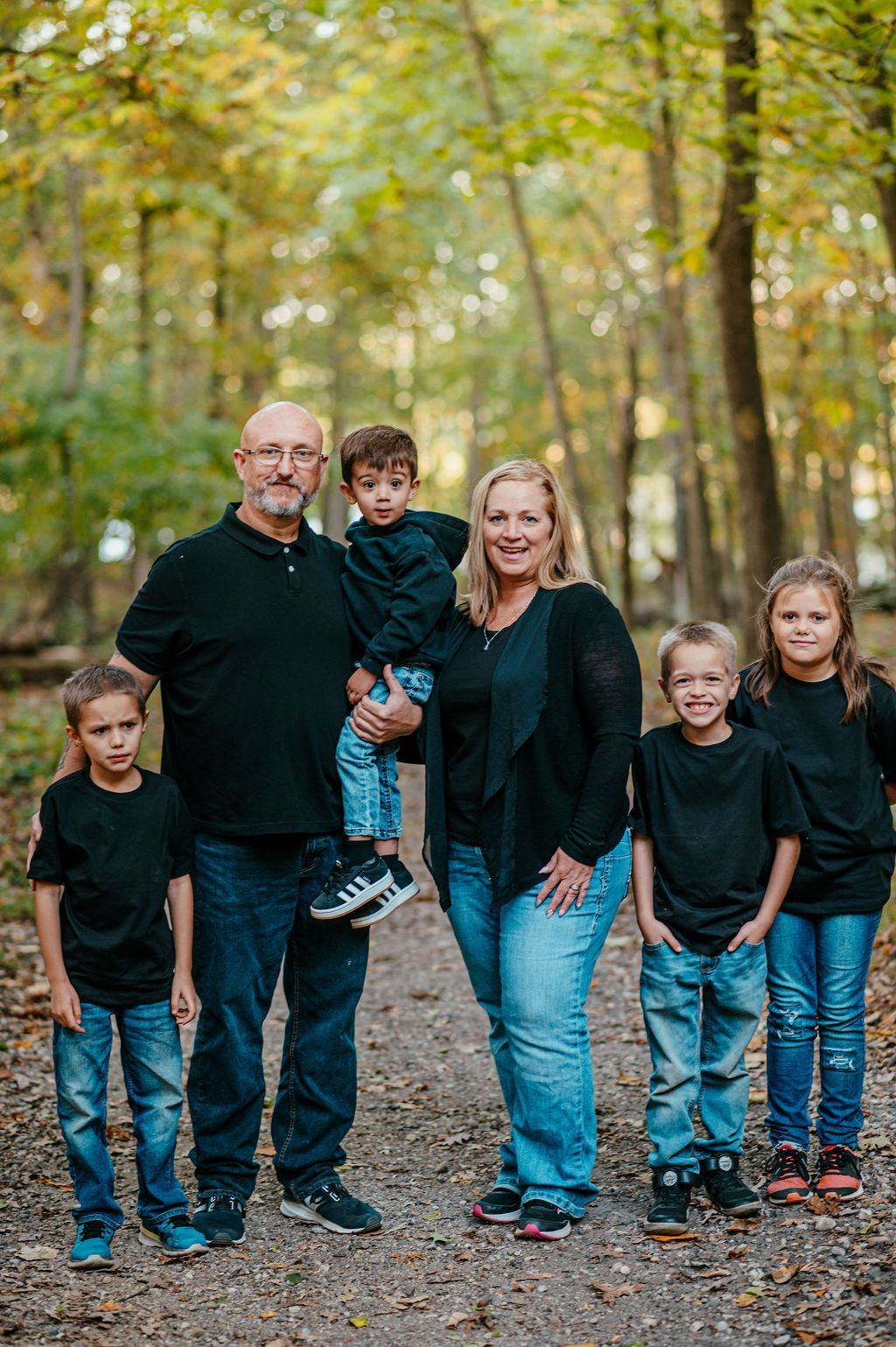 Family of five standing on a wooded path in autumn, dressed in dark tops and jeans.