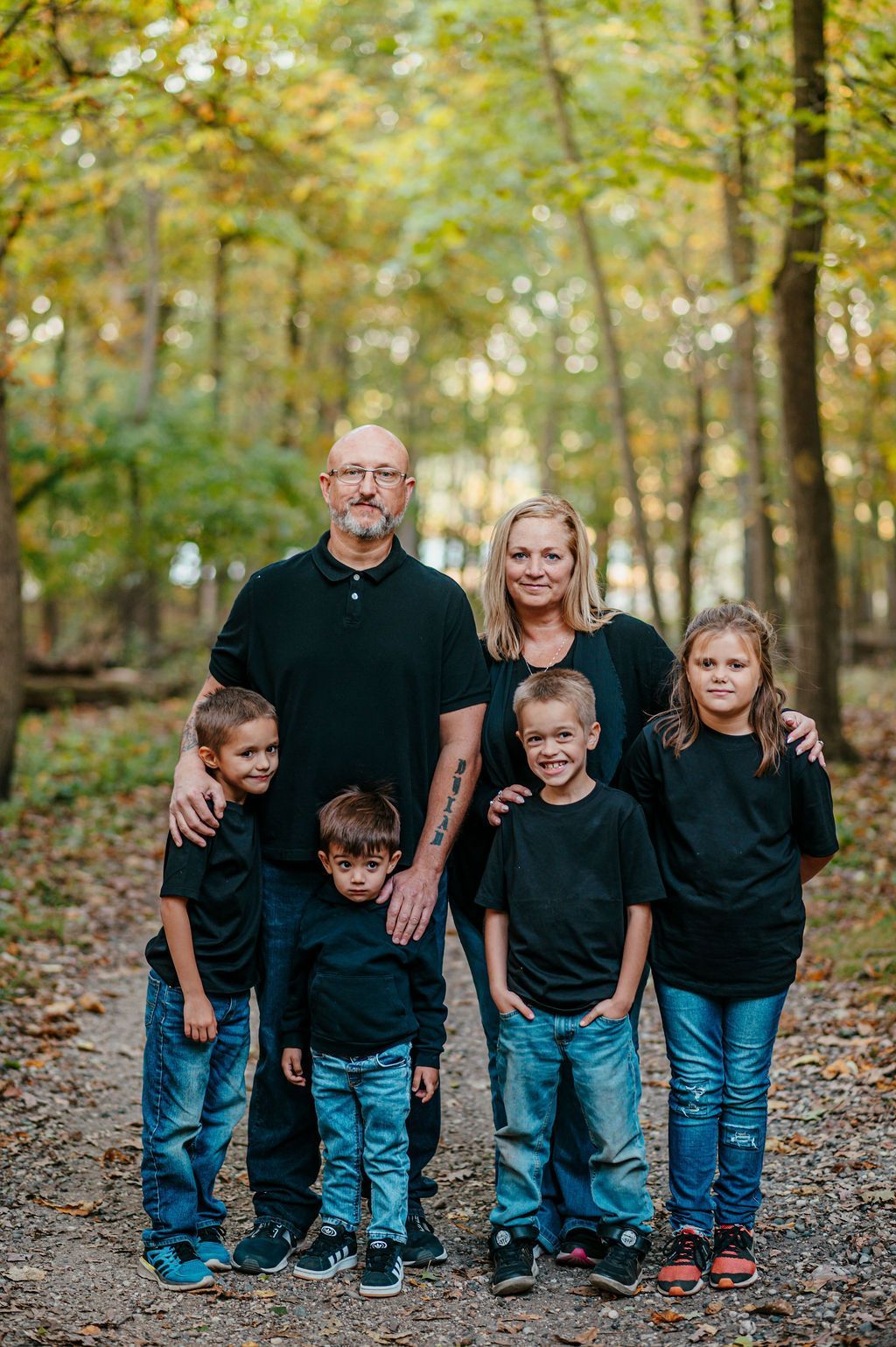 Family of five standing on a forest path, all wearing black tops and jeans, with autumn trees behind them
