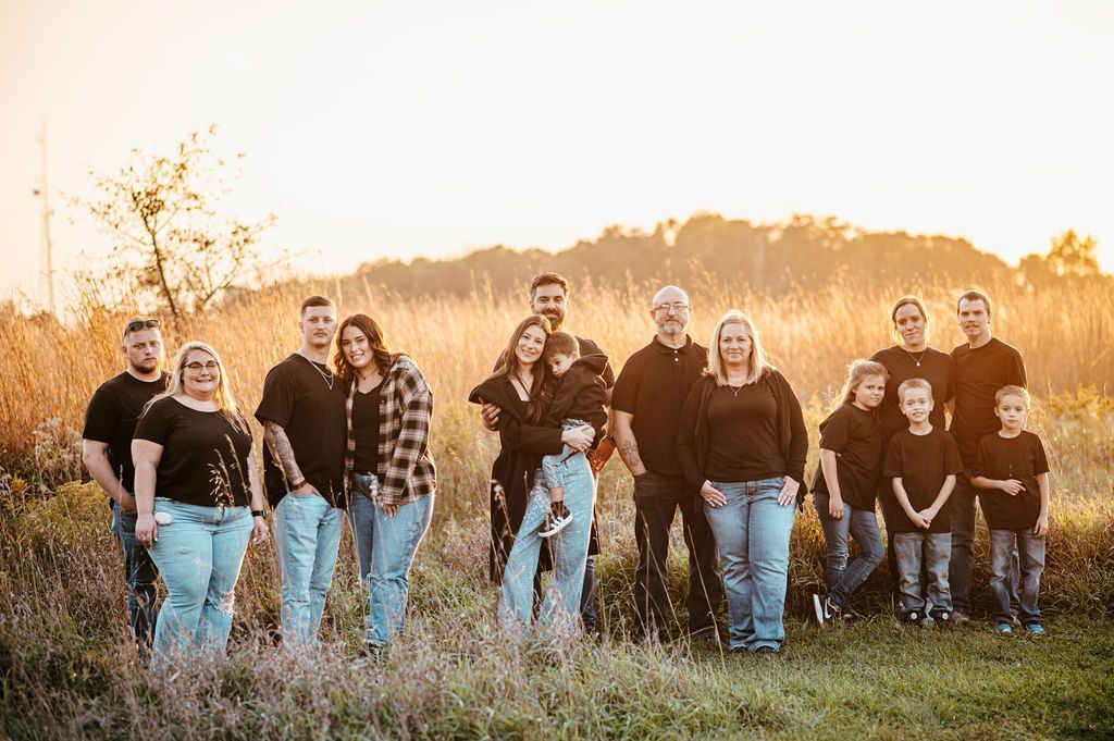 Group of people in casual clothes standing in a sunlit field at sunset, smiling at the camera