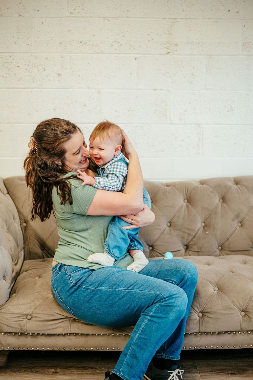 Woman holding a smiling baby on a beige couch against a white wall