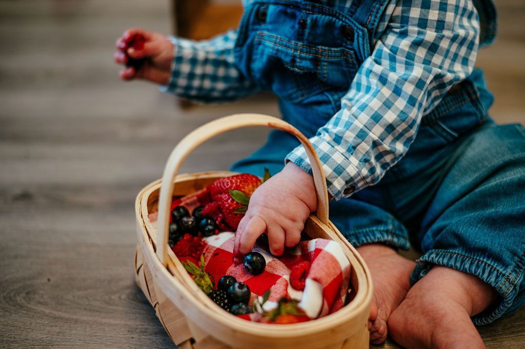 Child in denim overalls reaching into a basket of strawberries on a wooden floor