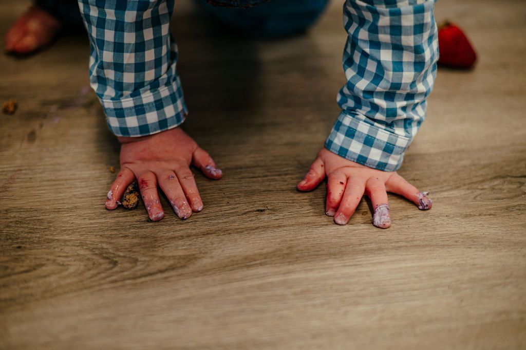 Hands on wooden floor, wearing blue checkered sleeves, with a red-tipped finger on one hand.