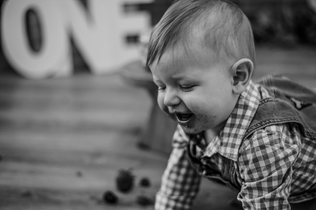 Black-and-white photo of a laughing baby crawling on a wooden floor near blurred letters in the background