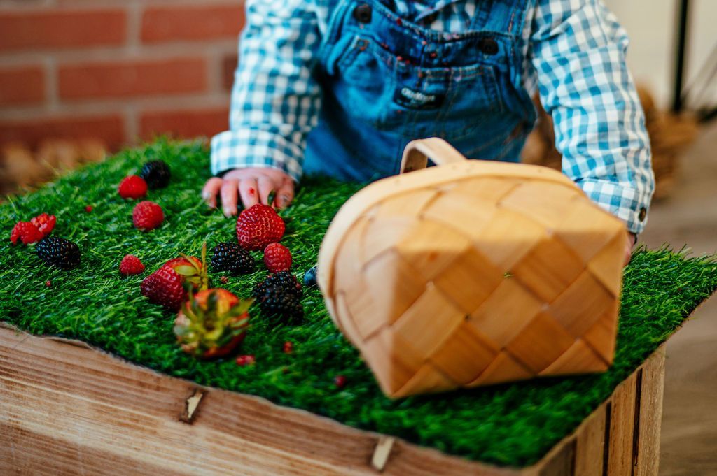 Child in blue plaid shirt arranging flowers in a wooden crate garden bed with a wicker basket nearby