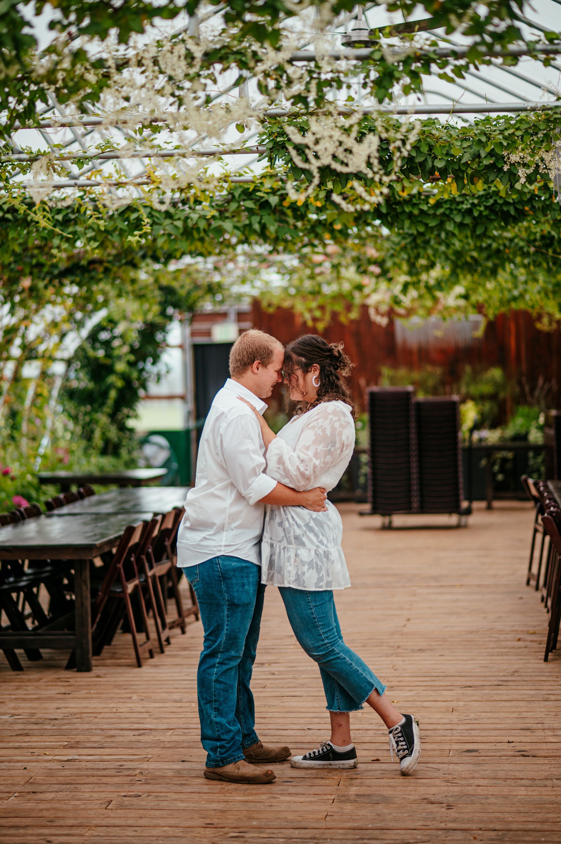 Couple embracing on a wooden deck under white flowers and greenery in an outdoor venue