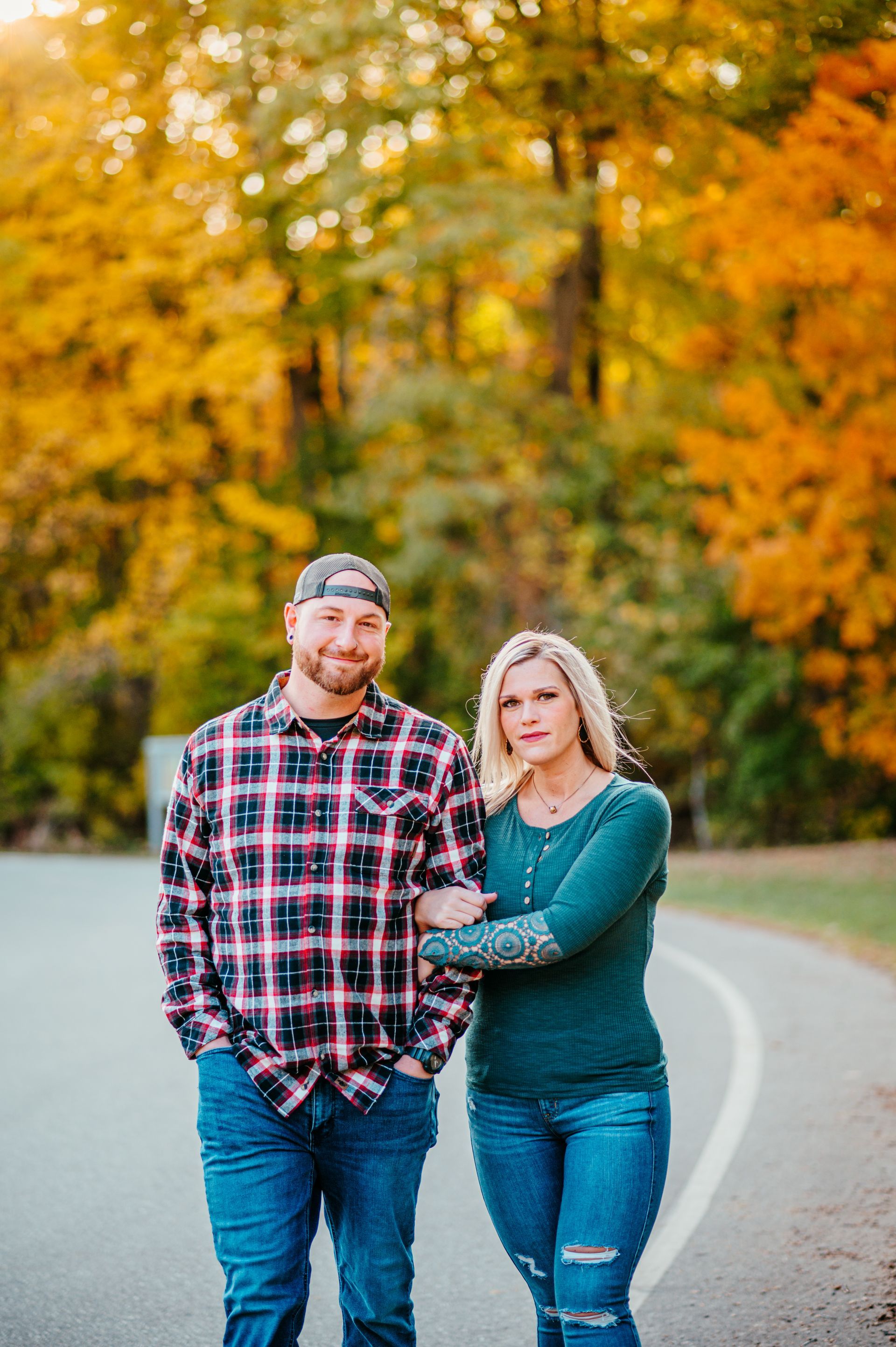 Two people standing on a curving road with autumn trees in the background