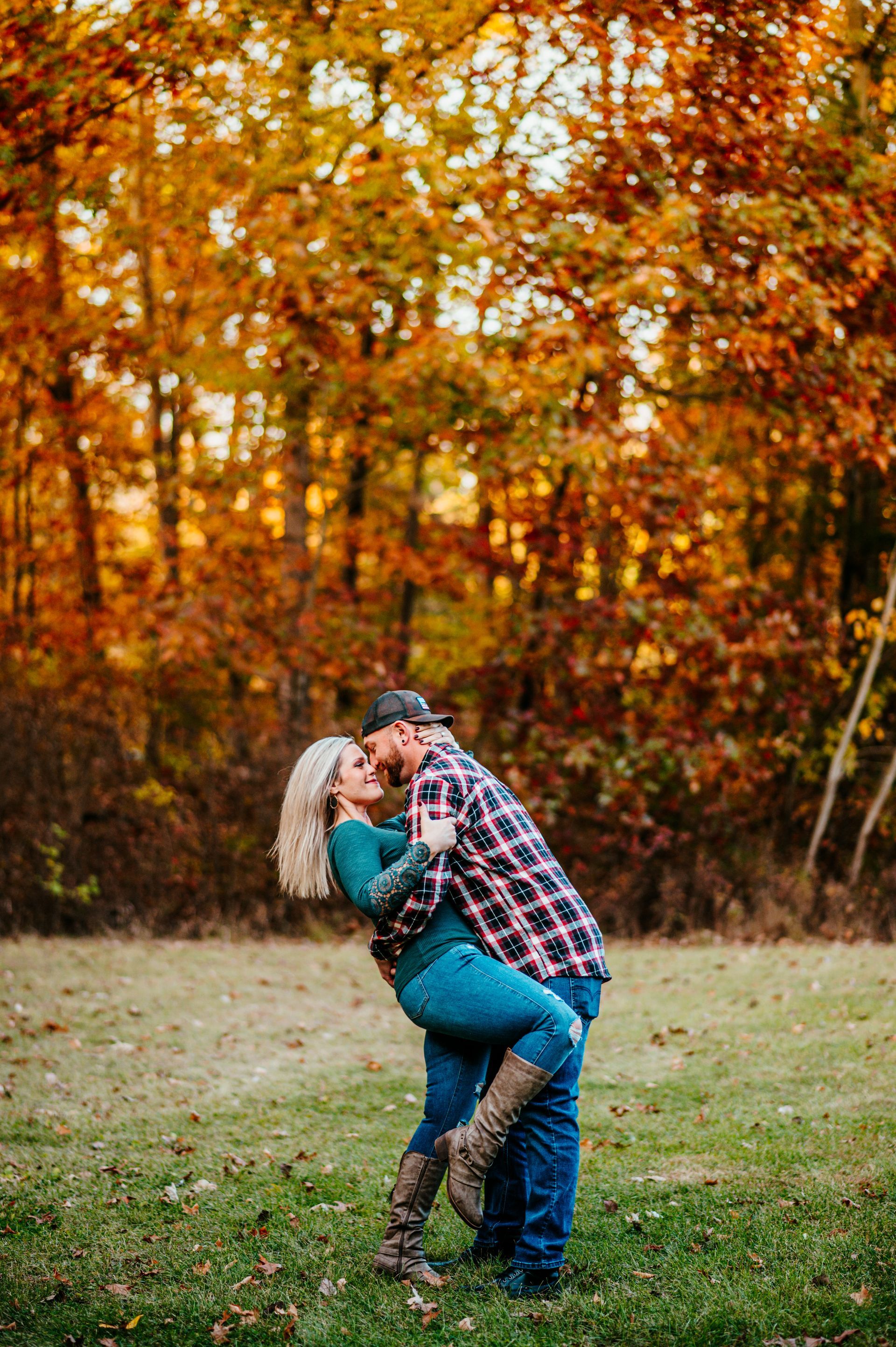 Couple embracing in a grassy field with autumn trees in the background