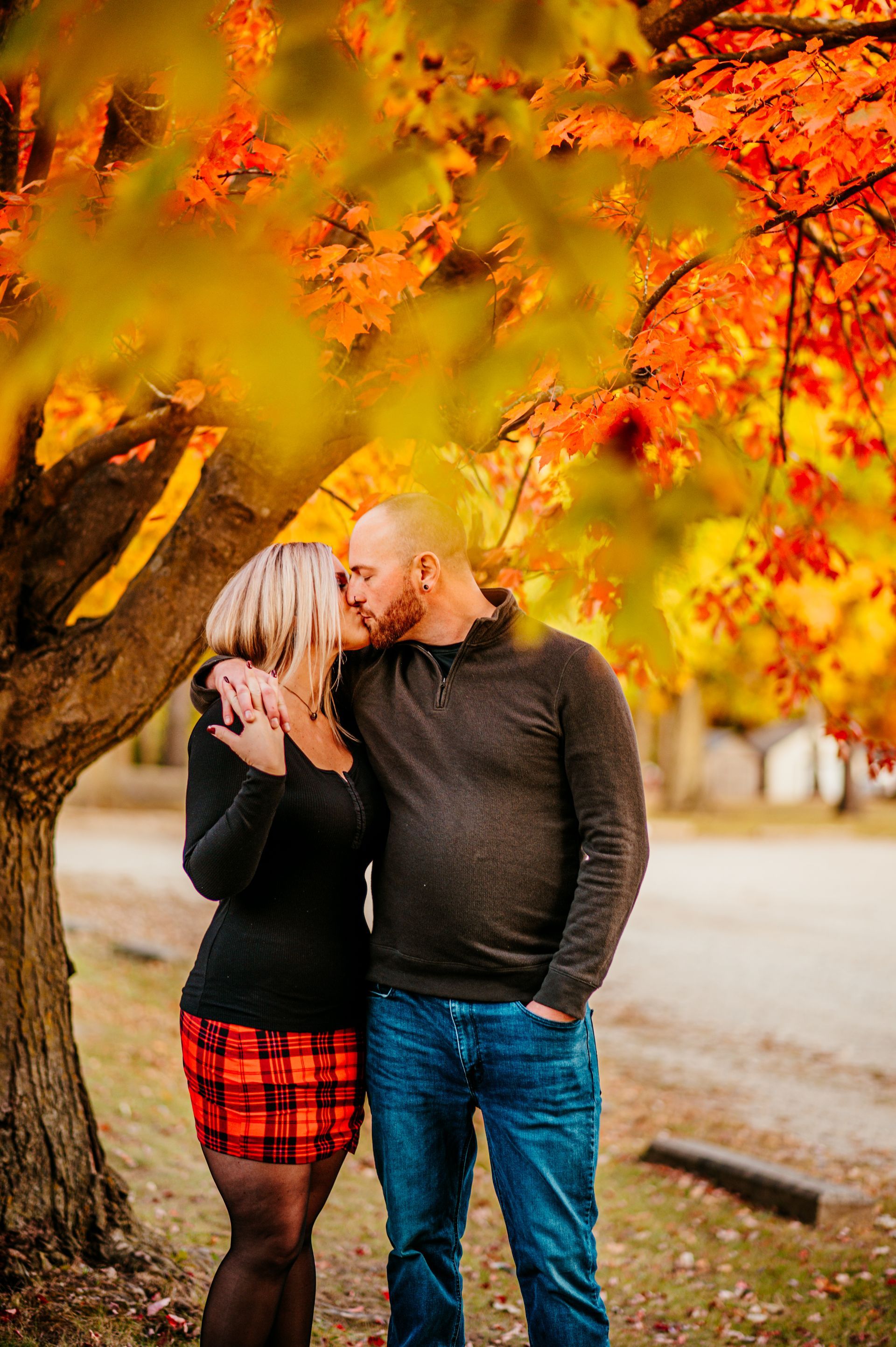 Couple kissing under autumn trees with bright orange leaves