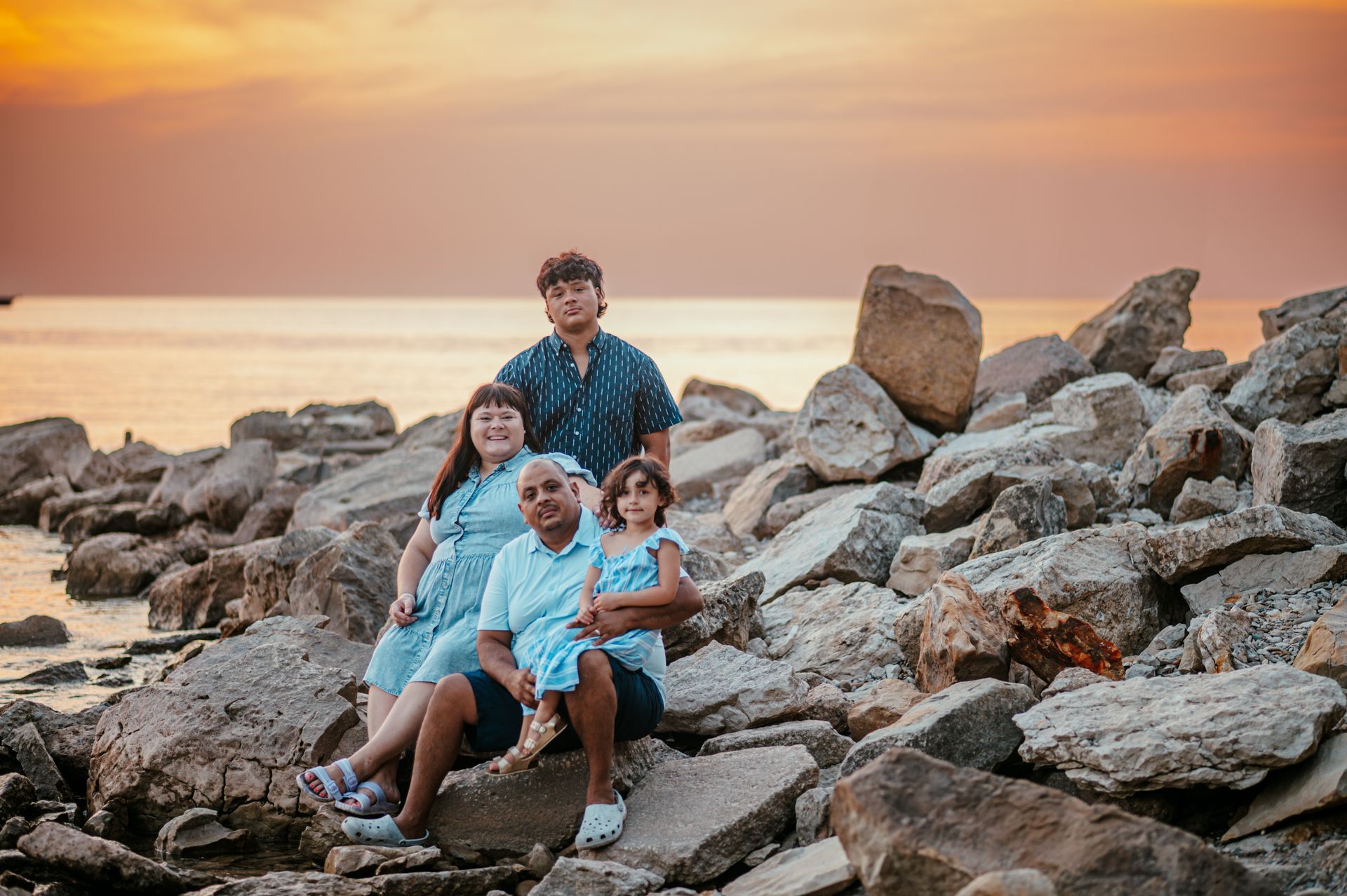 Family sitting on rocks at sunset by the sea