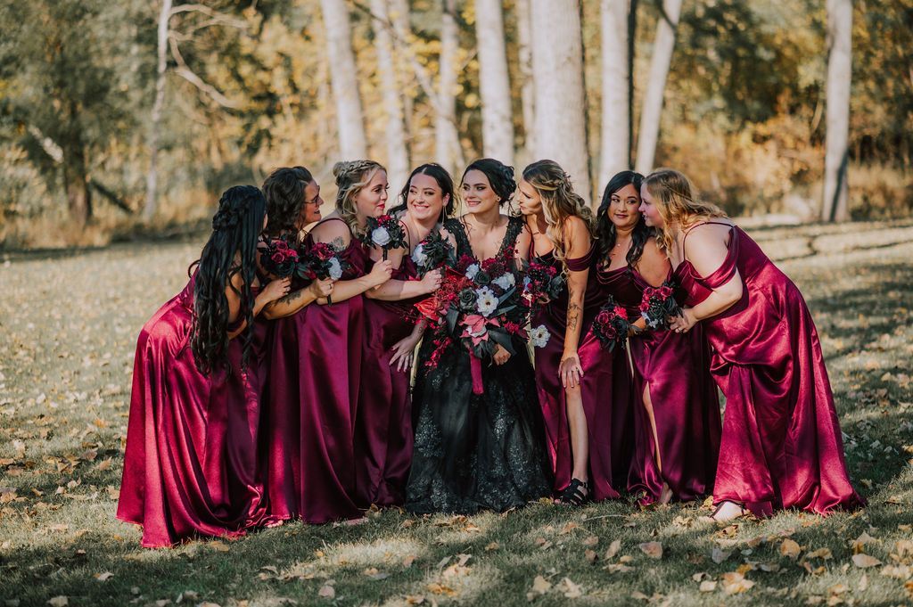Group of women in burgundy dresses and a black floral dress posing in a wooded outdoor setting