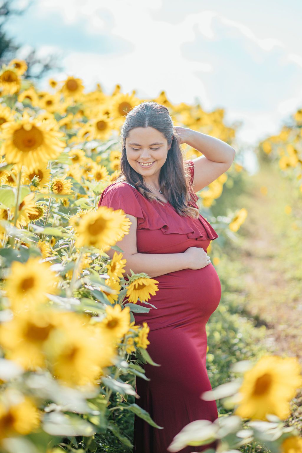 Pregnant woman in a red dress smiling in a sunflower field