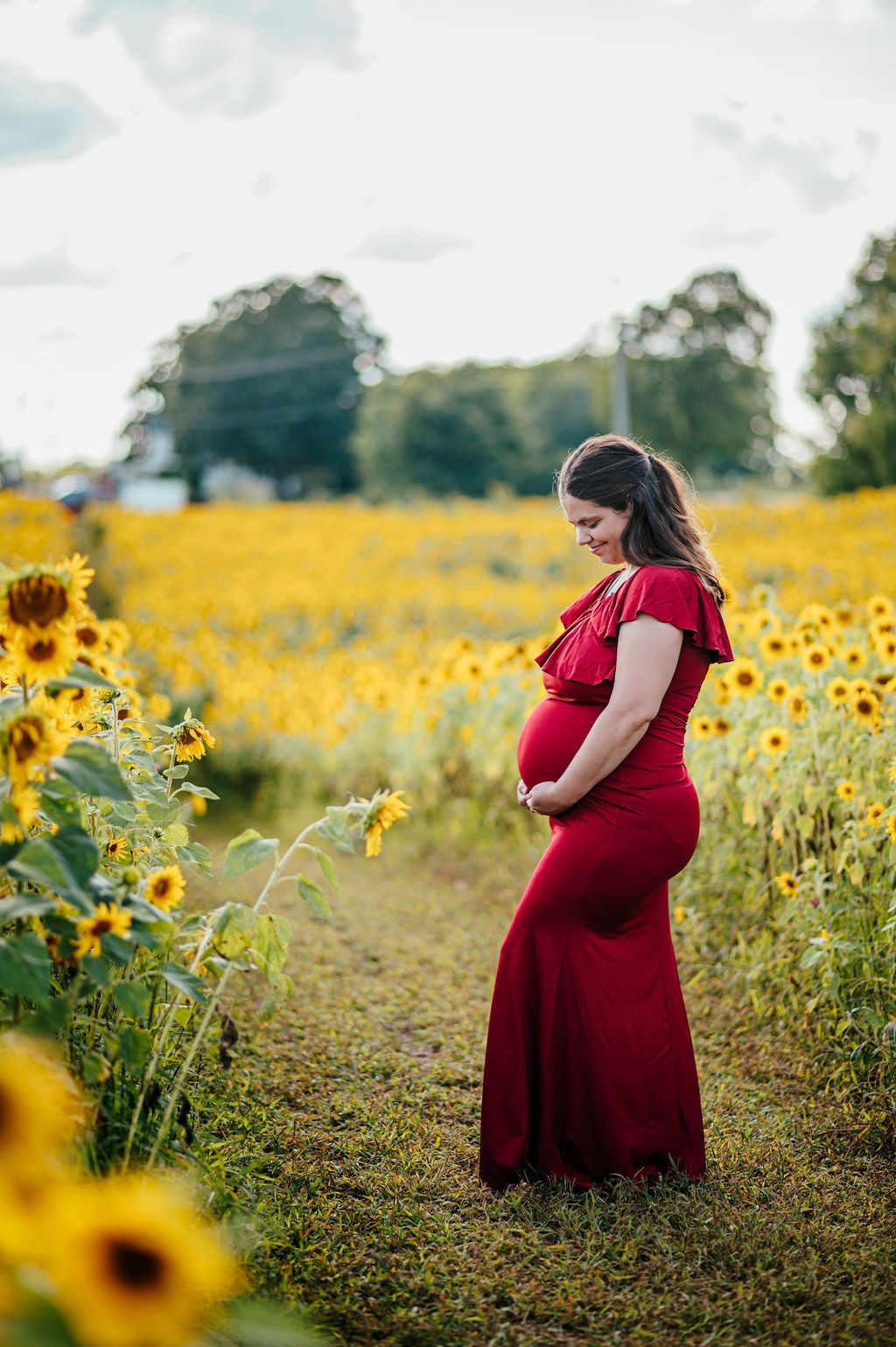 Pregnant woman in a red dress standing in a sunflower field