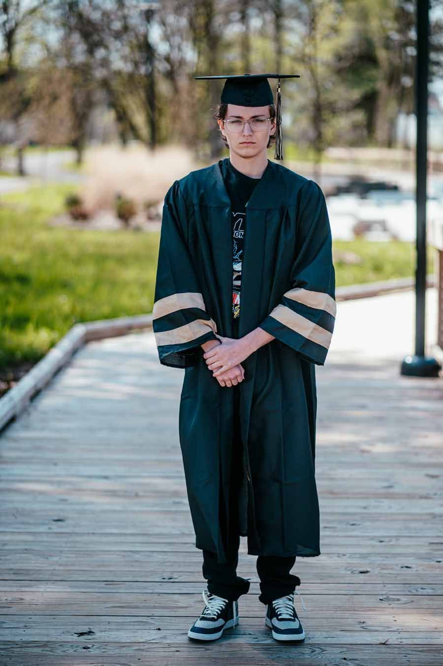 Graduate in black cap and gown standing on a wooden path outdoors