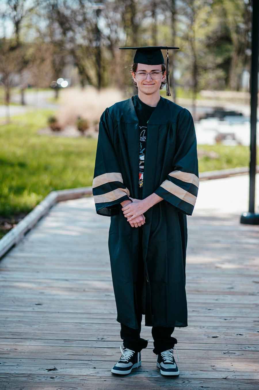 Person in graduation cap and gown standing outdoors on a path.