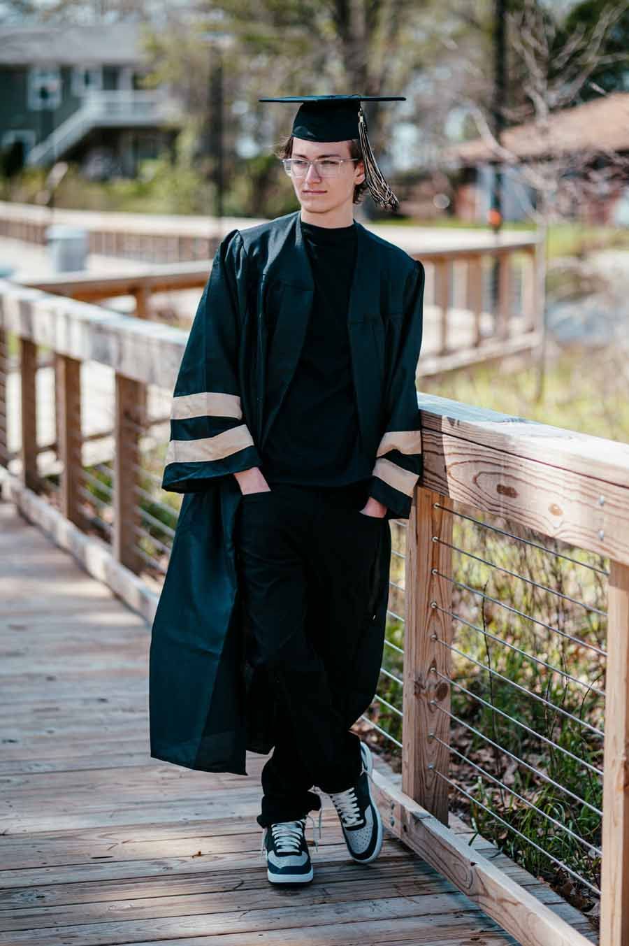 Person in graduation cap and gown standing on a wooden bridge outdoors