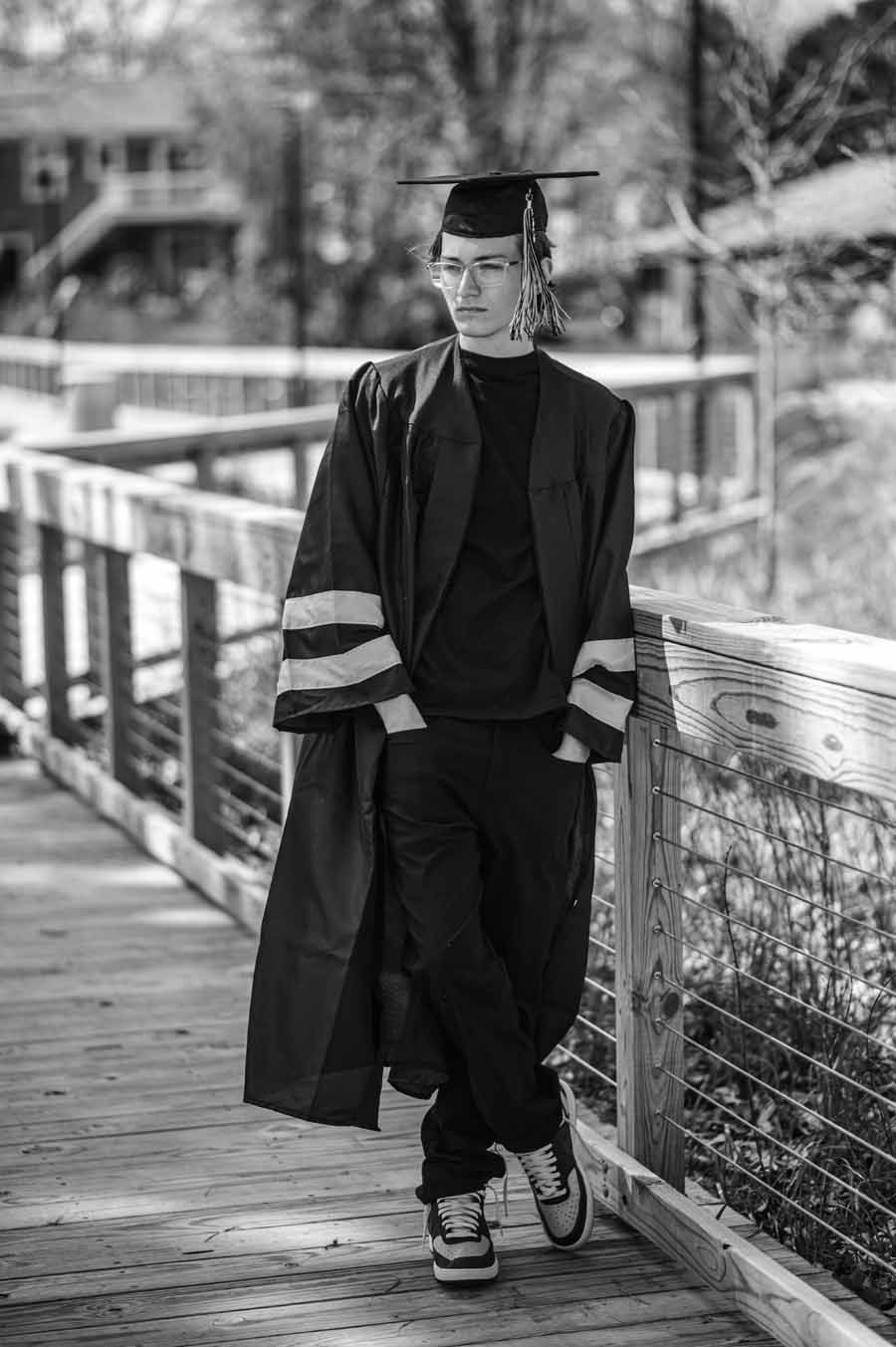 Person in graduation gown and cap standing on a bridge railing, holding a railing beside a canal.