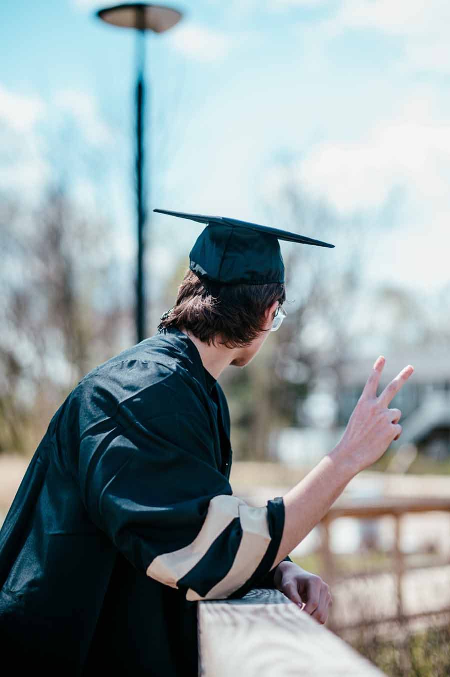 Graduate in black cap and gown looking back and flashing a peace sign outdoors