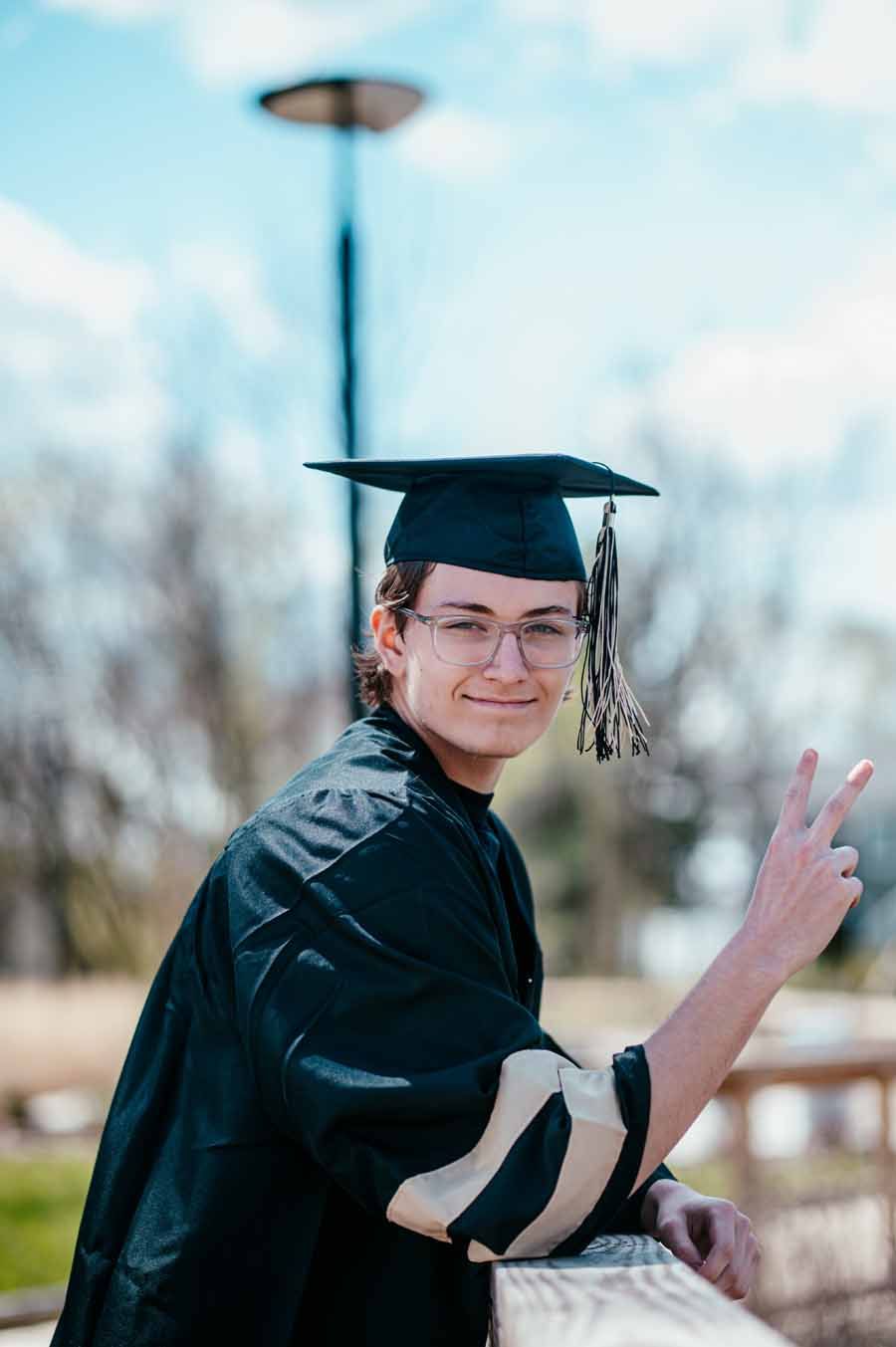 Graduate in cap and gown smiling and making a peace sign outdoors
