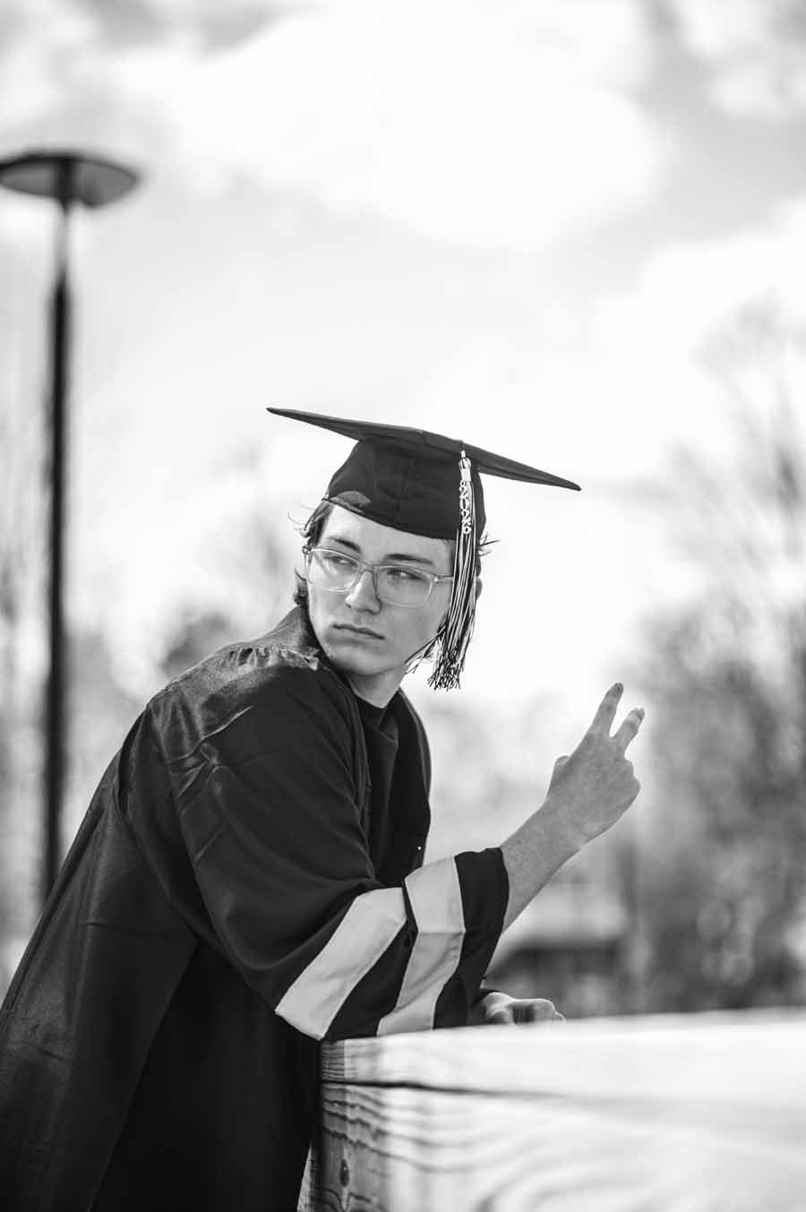 Graduate in cap and gown turns back and flashes a peace sign outdoors.