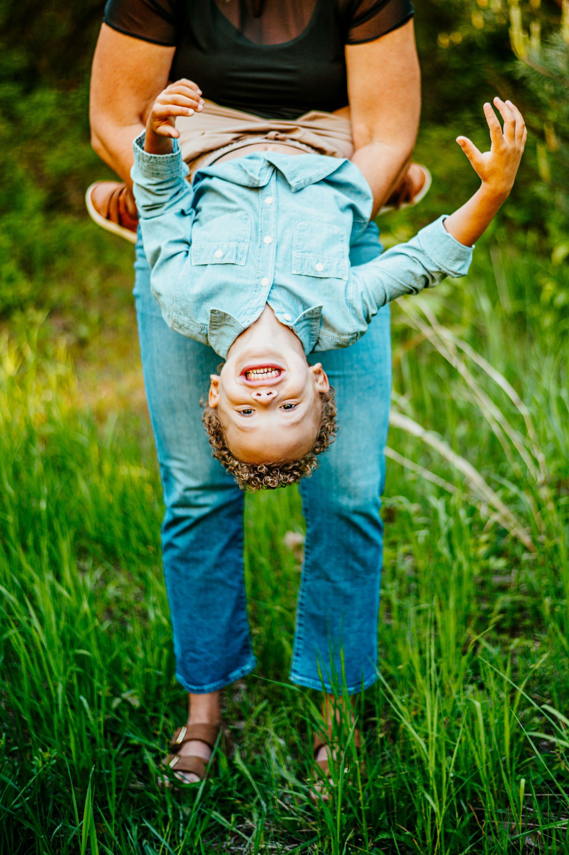 Person holding a smiling child upside down in a grassy field