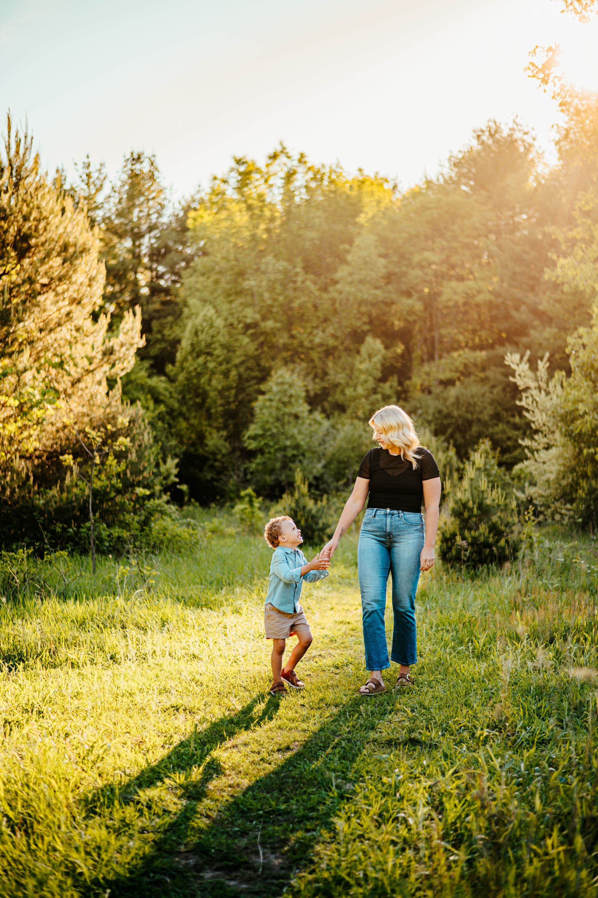 Adult and child walking hand-in-hand on a sunlit grassy path beside trees