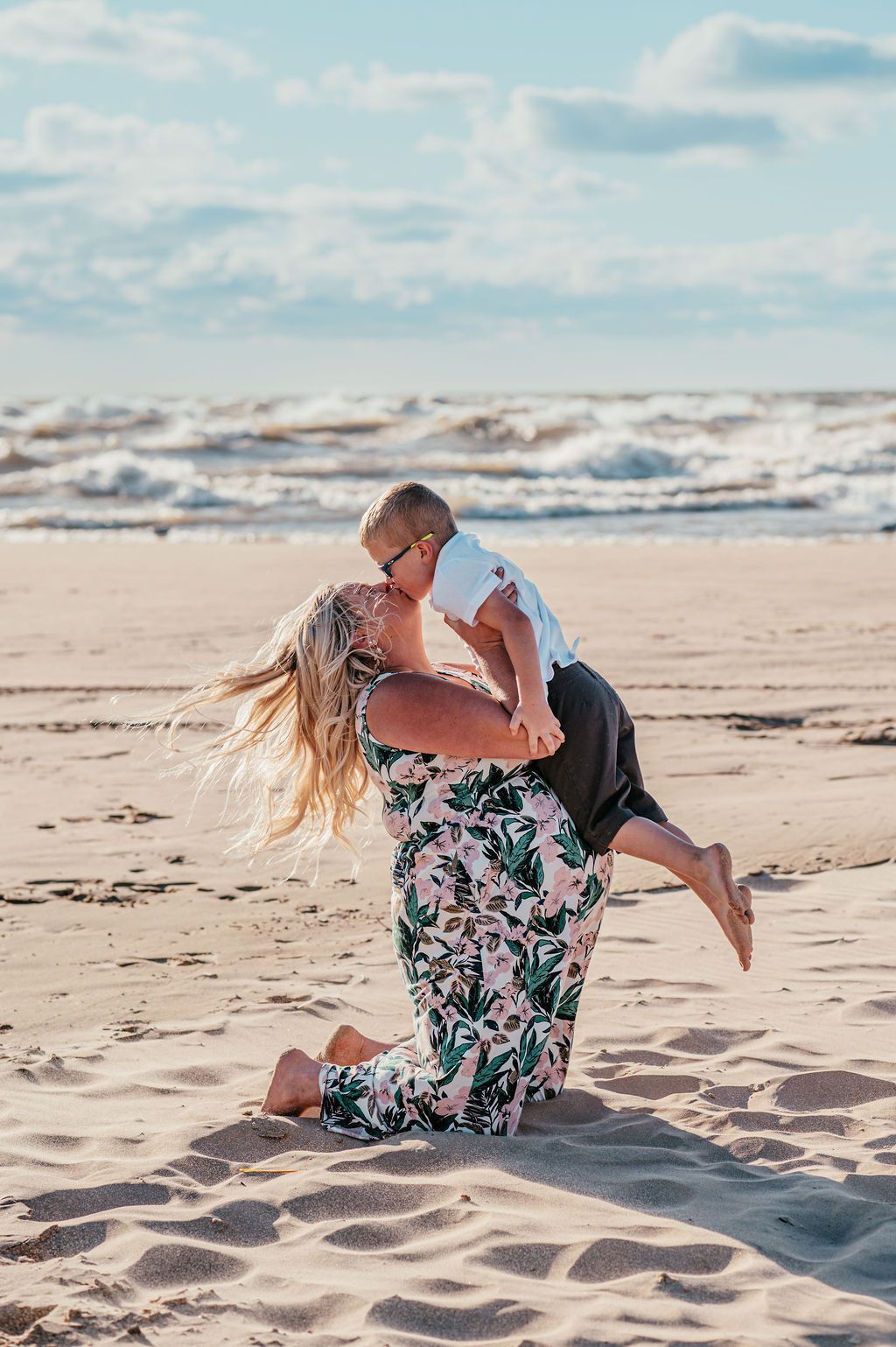 Couple kissing on a sandy beach, with ocean waves and cloudy sky in the background