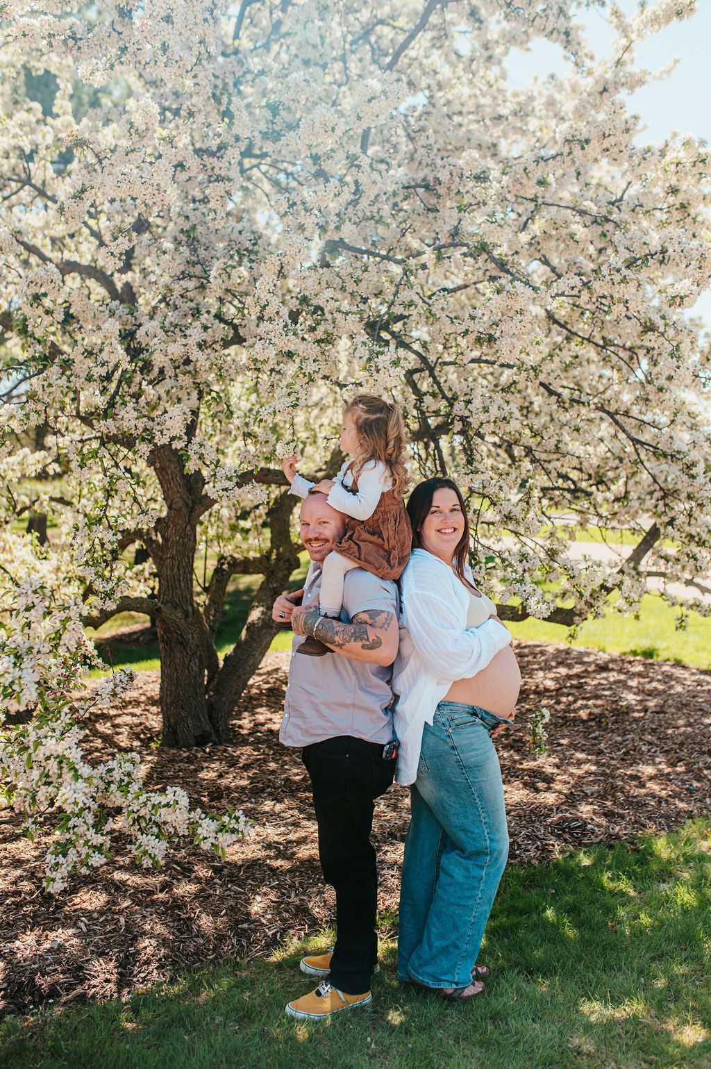 Three people posing under a blooming tree in a sunny park.