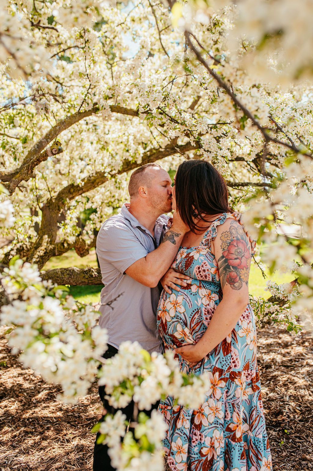 Couple embracing under blooming white blossoms in a sunlit orchard