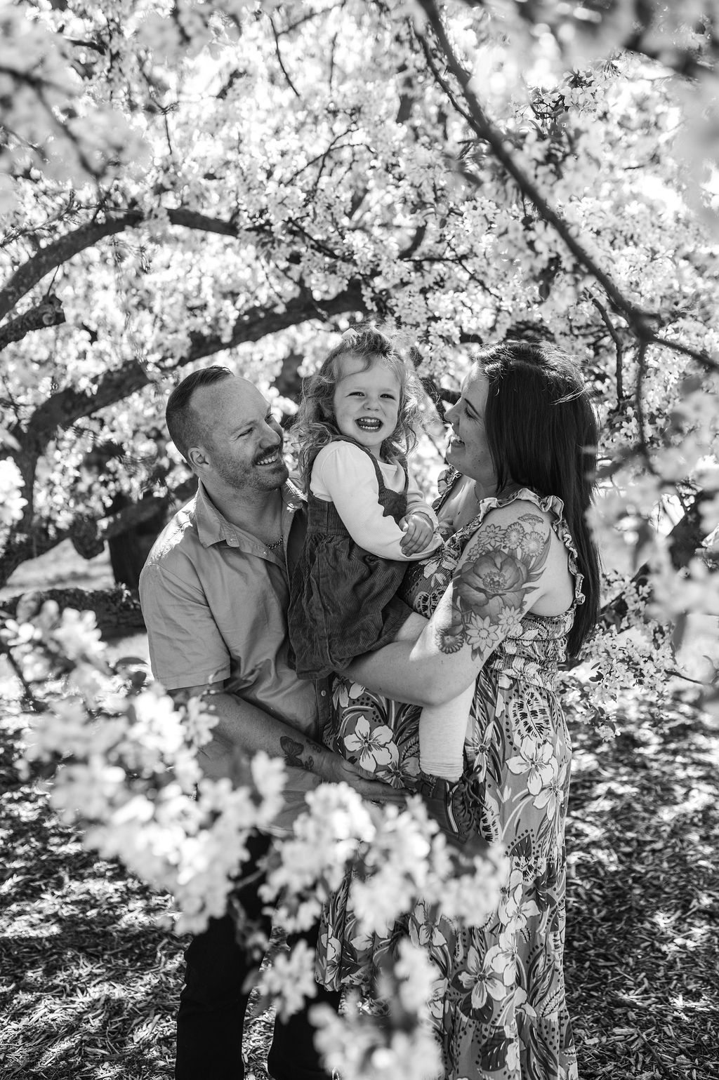 Family smiling among flowering tree branches in black-and-white portrait