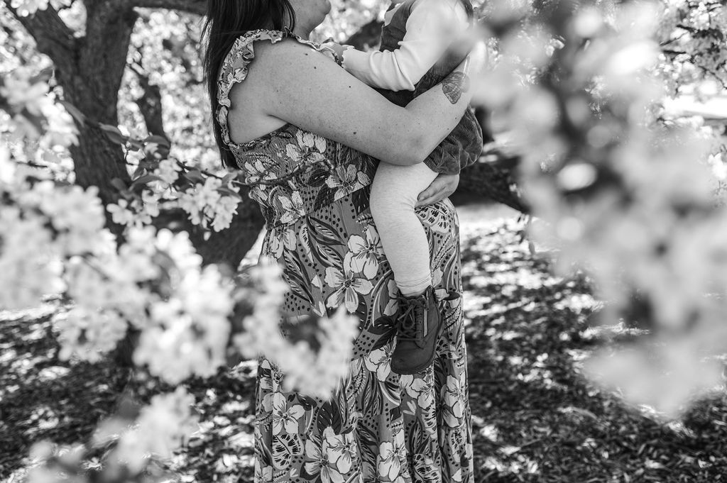 Black-and-white photo of a person holding a baby among blooming flowers outdoors