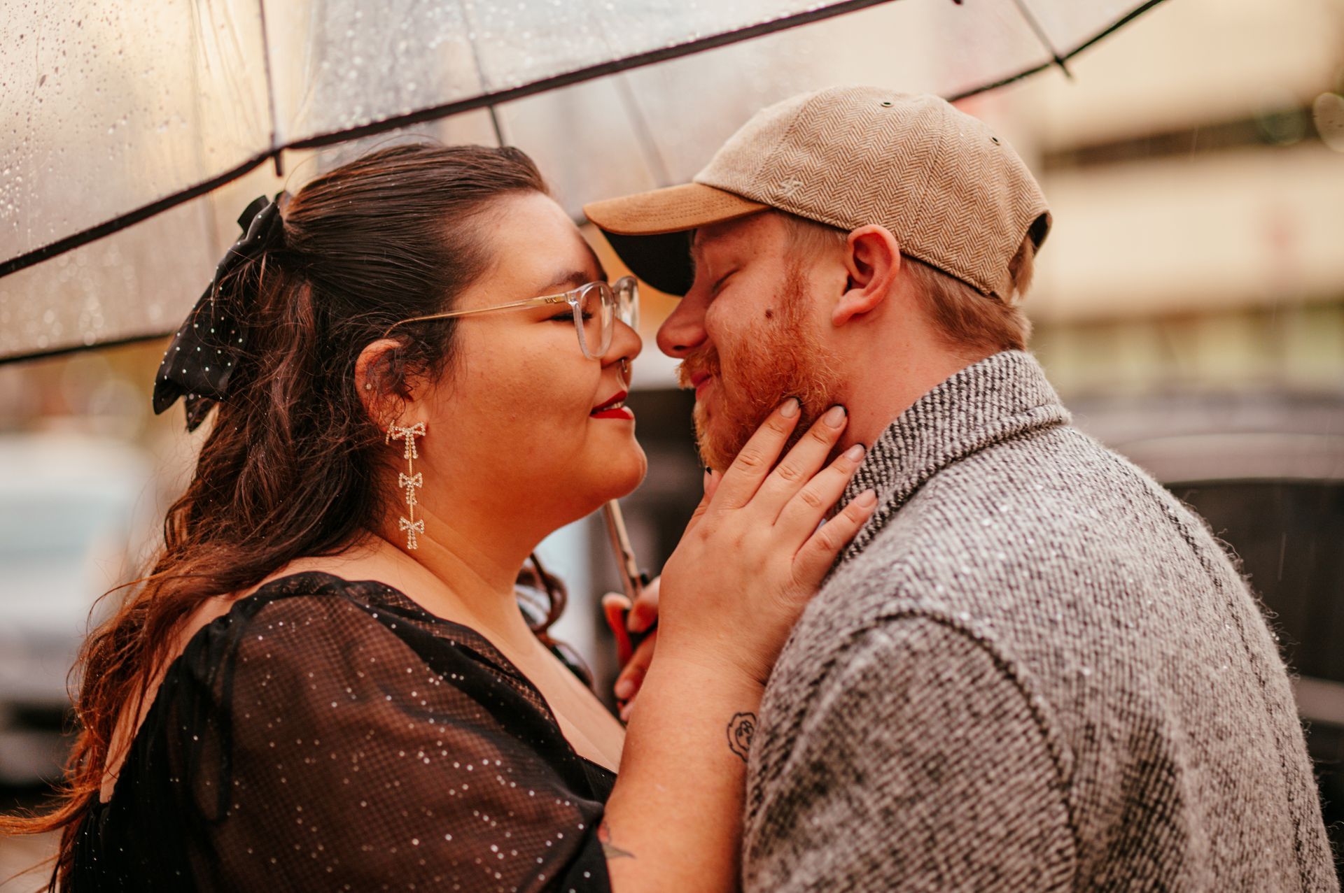 Two people stand close, touching faces and smiling under warm string lights.