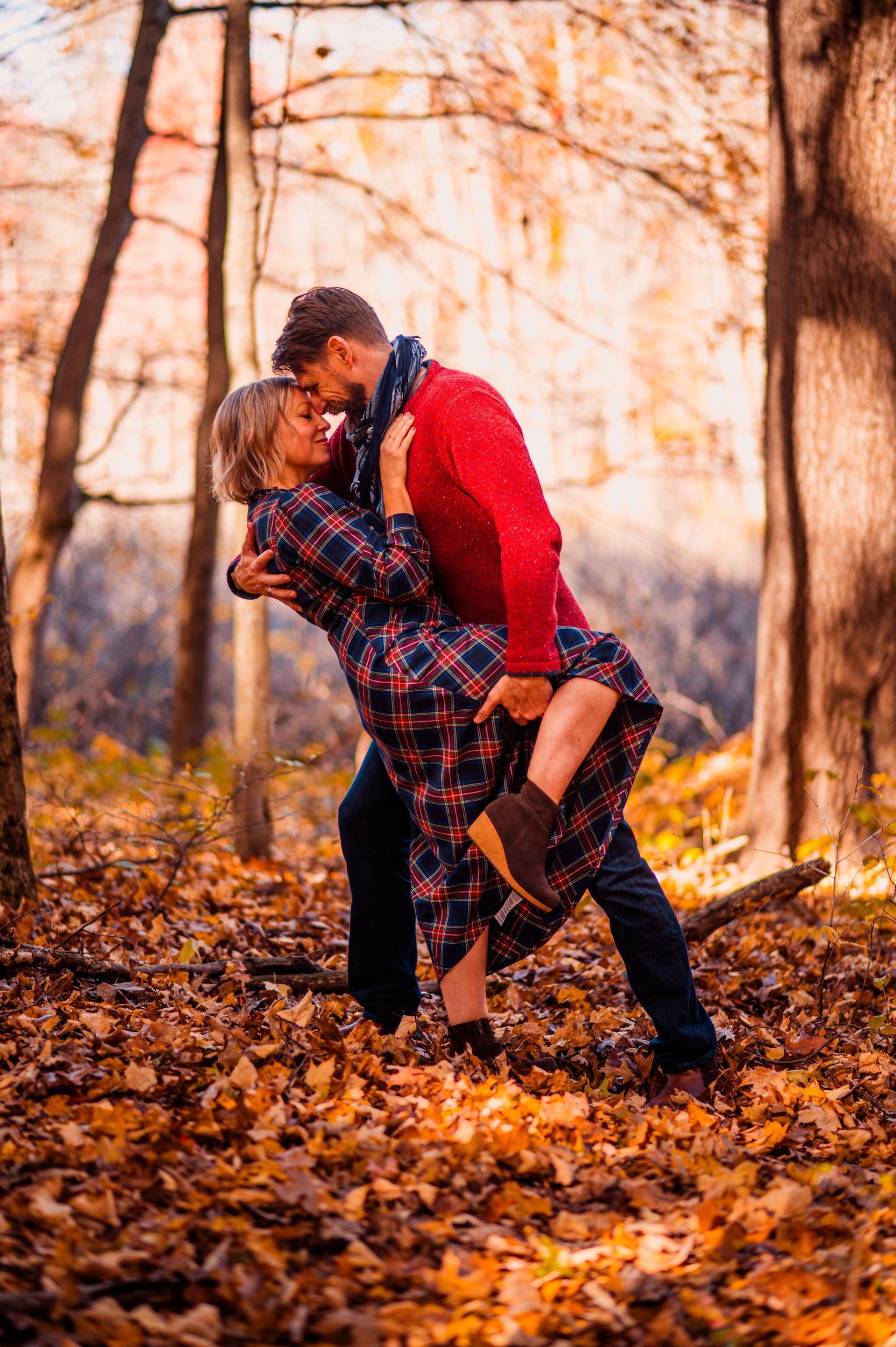 Couple embracing in a sunlit autumn forest, surrounded by fallen orange leaves.
