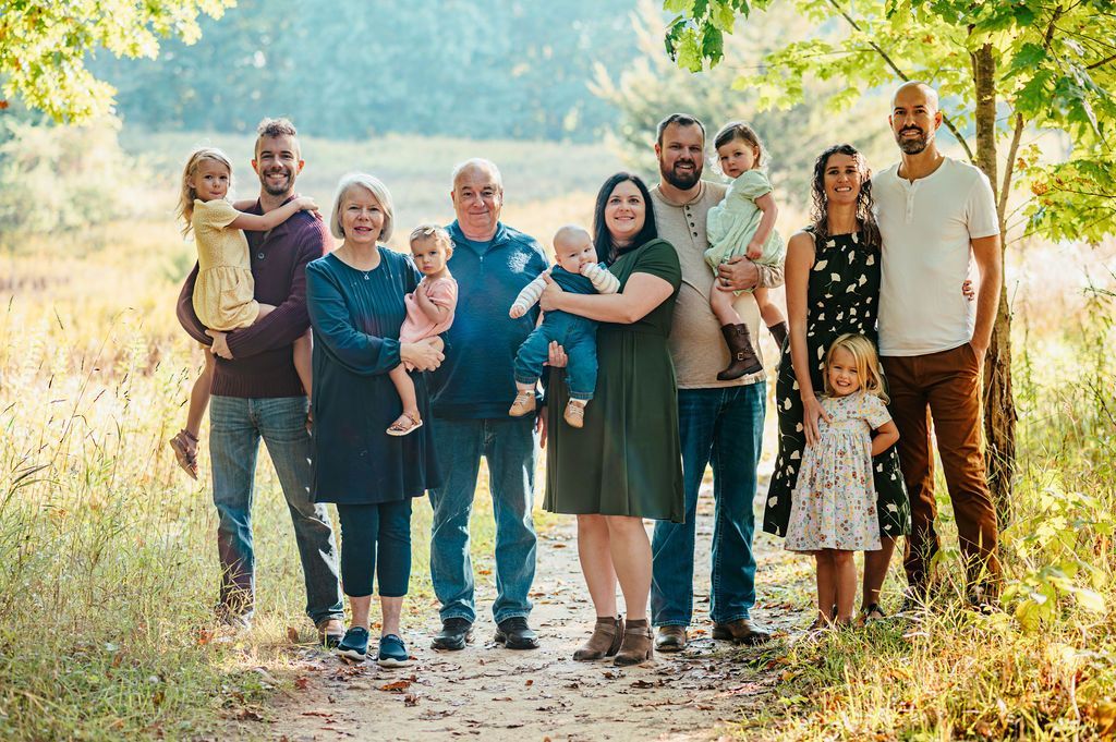 Group of people standing together outdoors in a sunlit field, smiling and posing for a family photo.