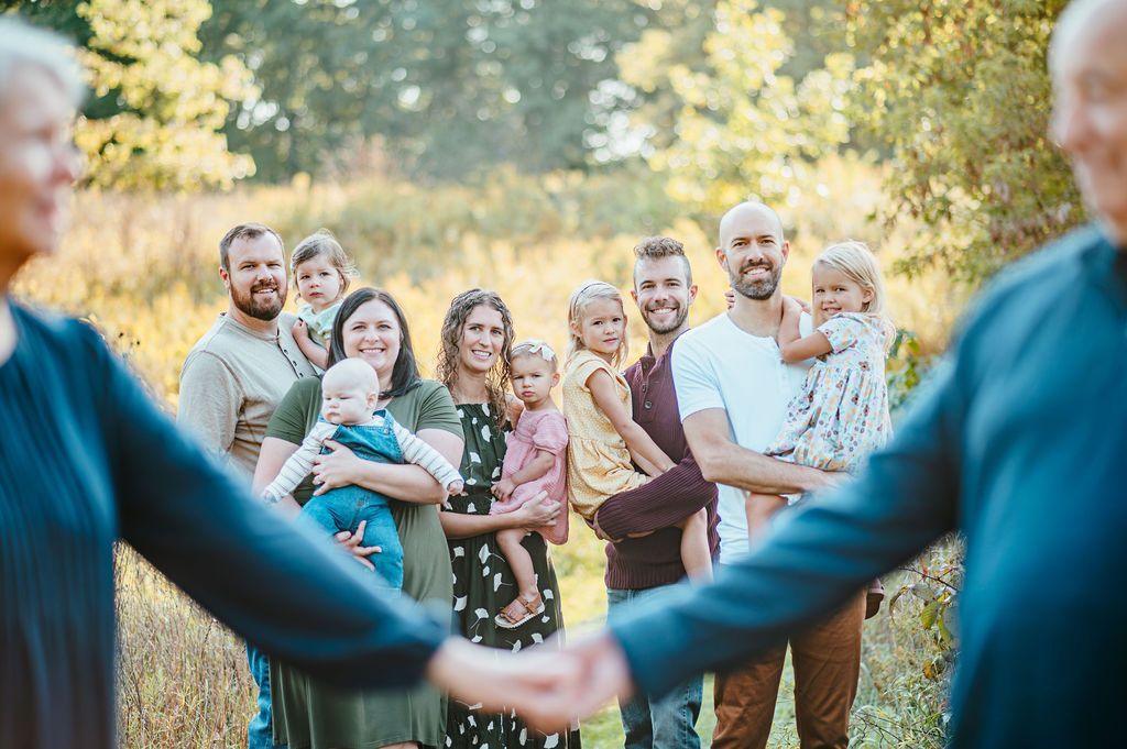 Group holding hands in a sunny outdoor circle, smiling in a garden.