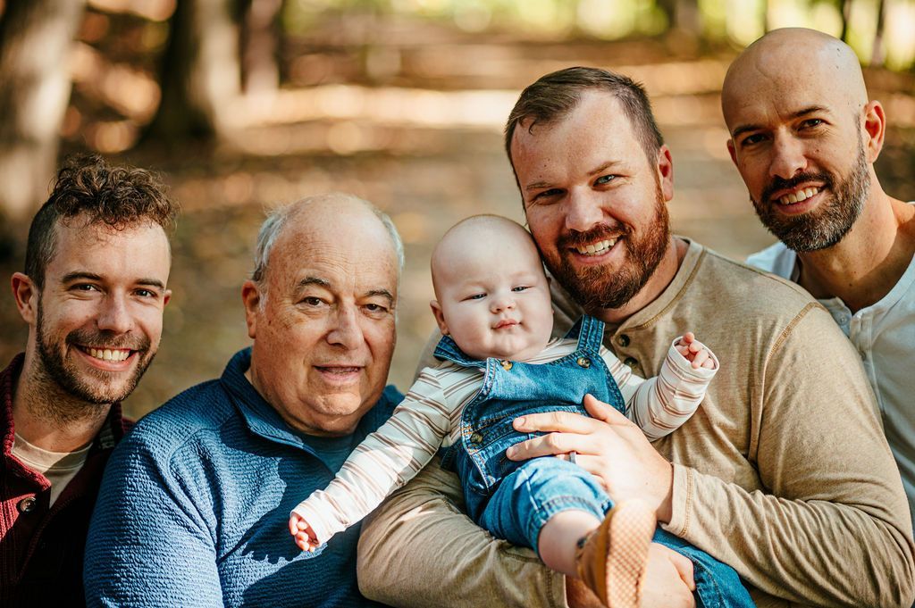 Five people pose closely together indoors, with one holding a baby in blue clothing.