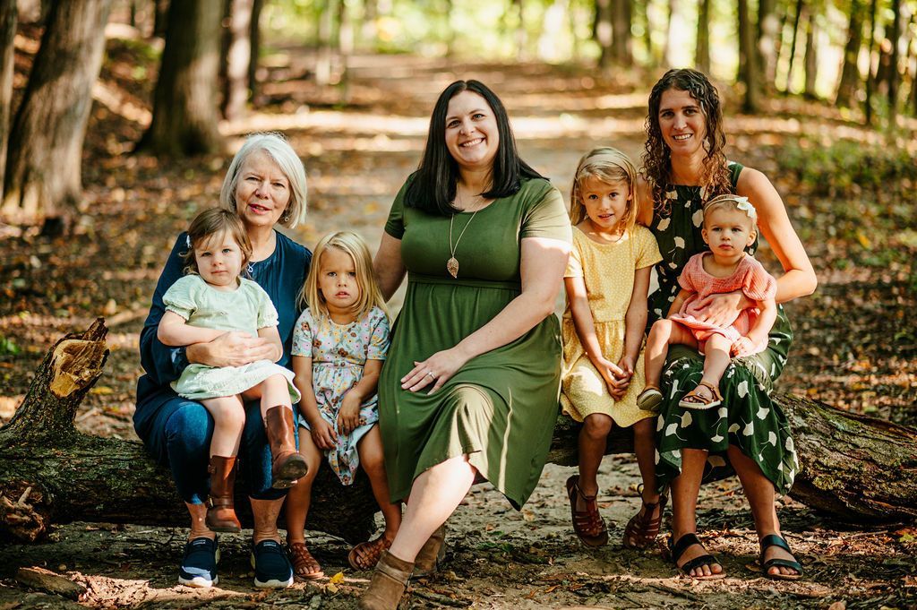 Six people seated on a bench in a wooded park, smiling at the camera.