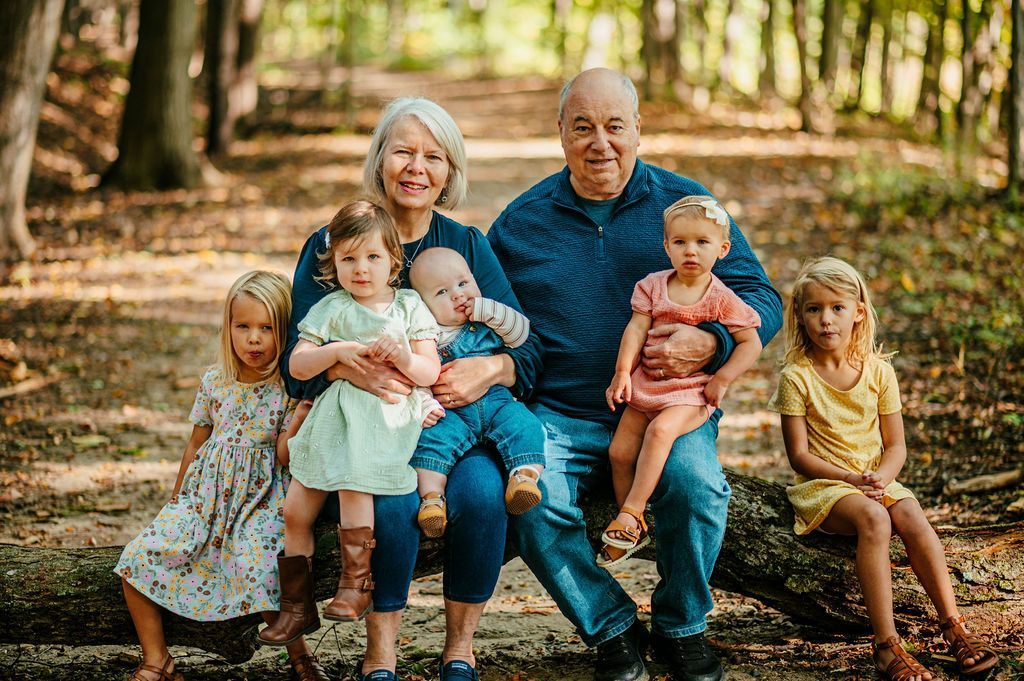Family seated on a forest path, with grandparents holding five young children, smiling at the camera
