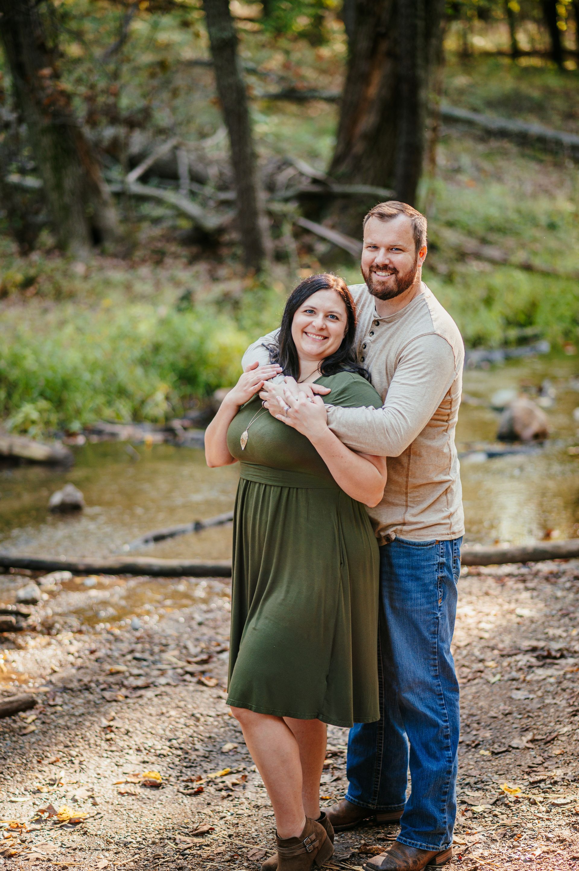 Couple embracing by a creek in a wooded outdoor setting