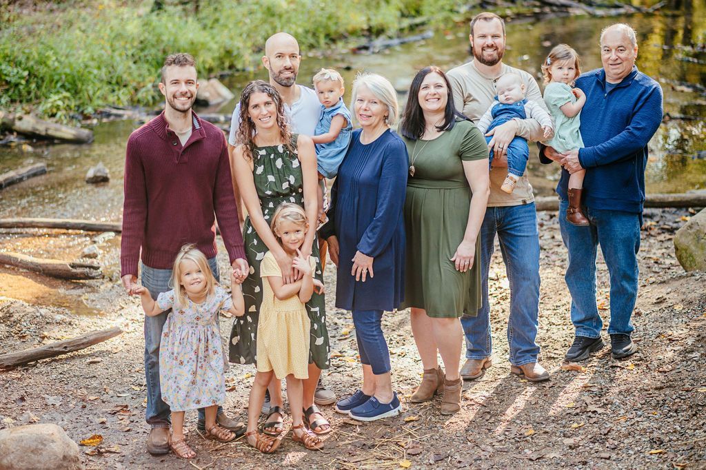 Family group posing outdoors on a gravel path beside a stream with trees in the background.