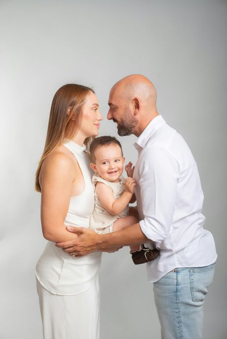 Family of three smiling and holding each other against a light gray background