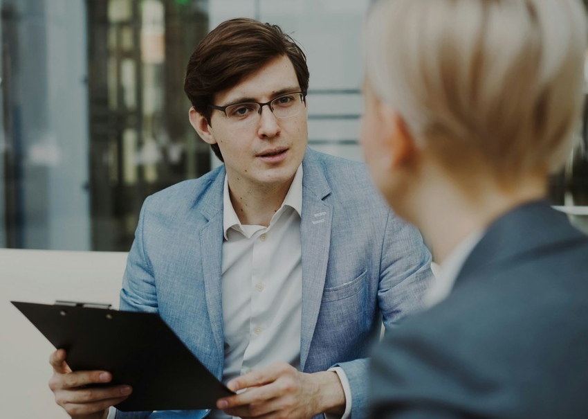 Two people in a free consultation meeting, one holding a clipboard and speaking across a table.